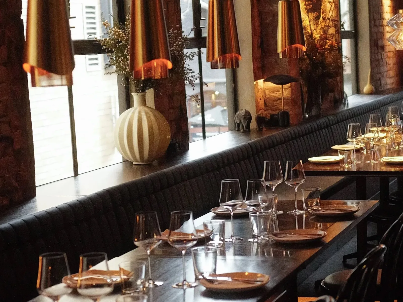 Embla wine bar interior with brass pendant lights, dark banquette and set tables