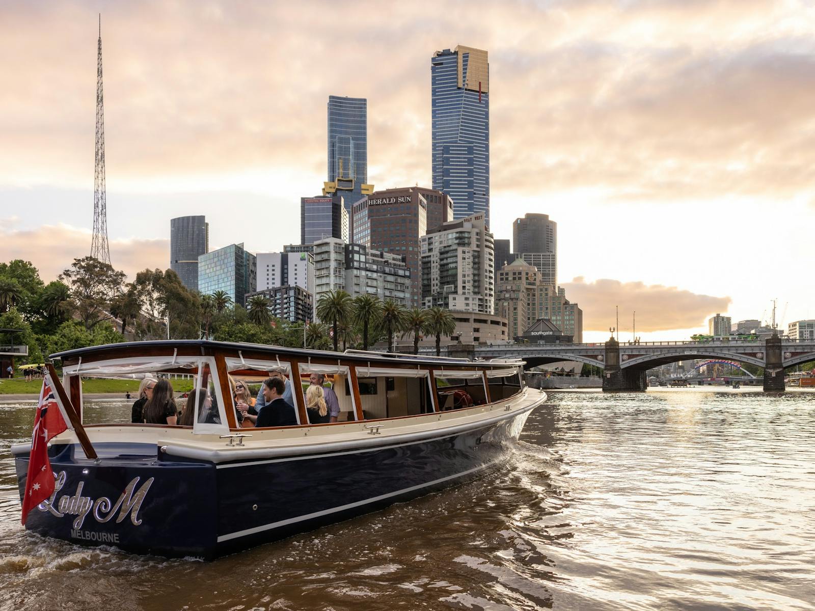 The Lady M boat cruising on the Yarra River with the Melbourne city skyline behind it