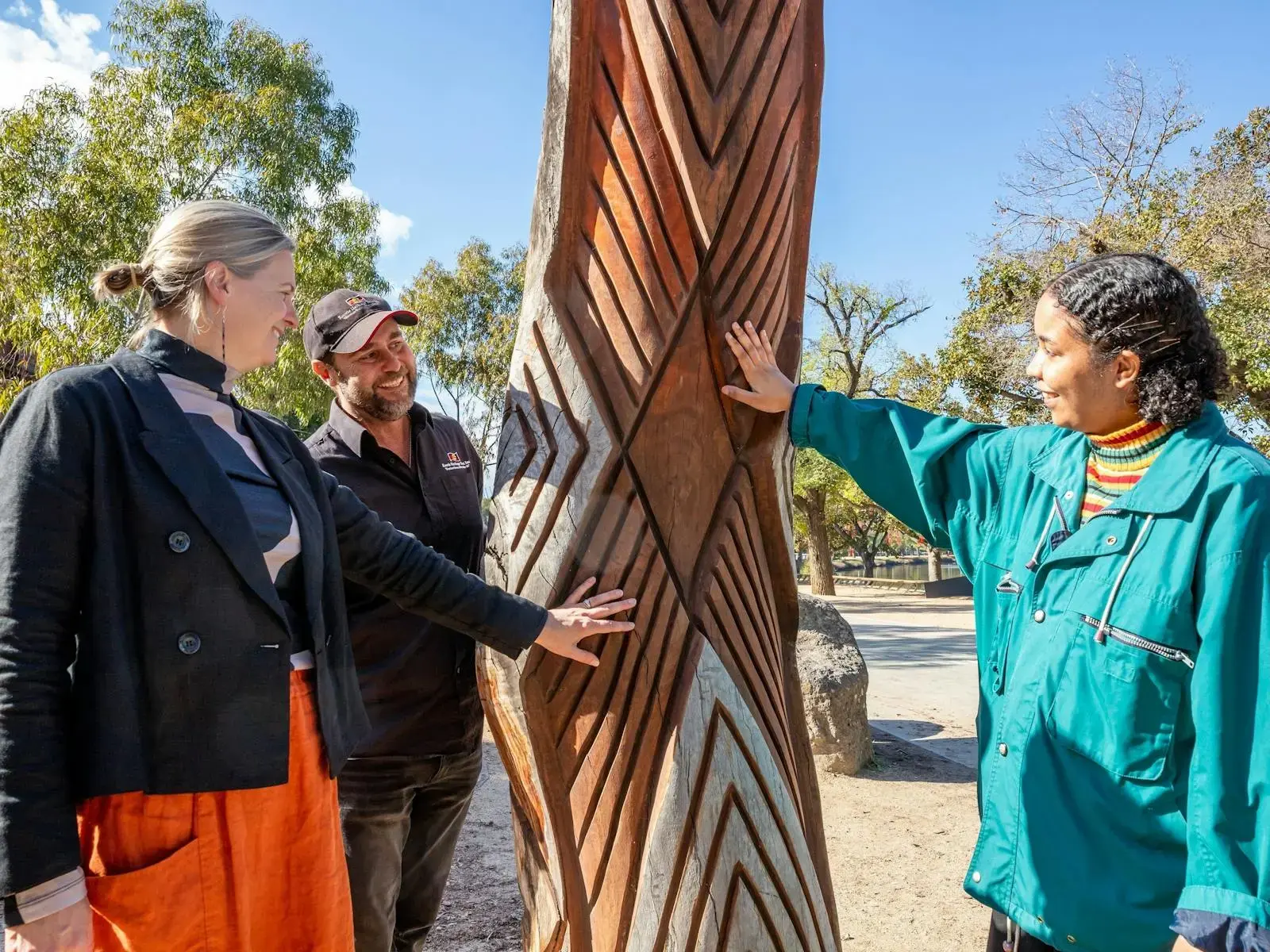 A First Nations guide showing visitors a large carved wooden sculpture outdoors at Koorie Heritage Trust.