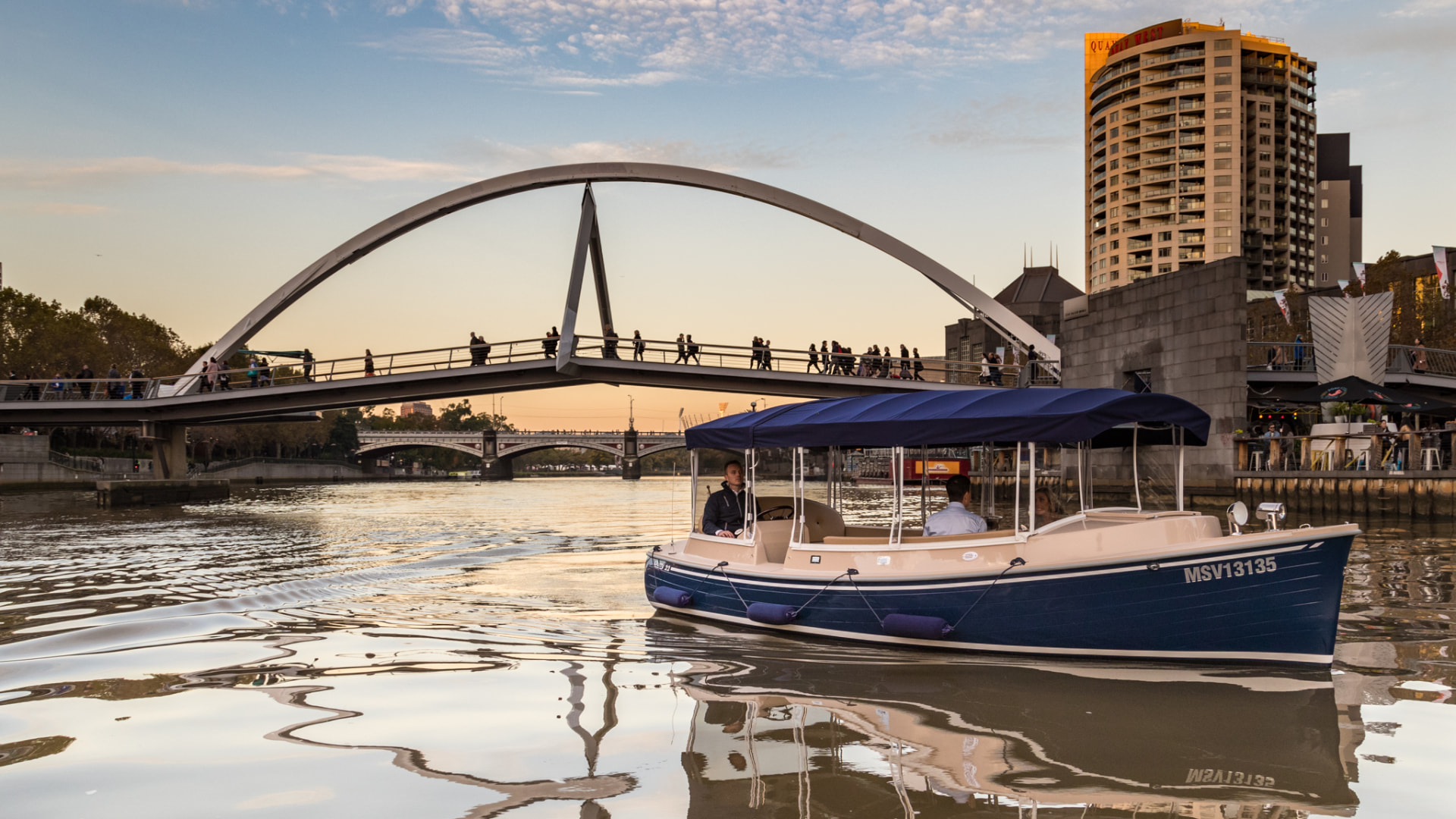 A private electric boat on the Yarra River beneath the Evan Walker Bridge at sunset.