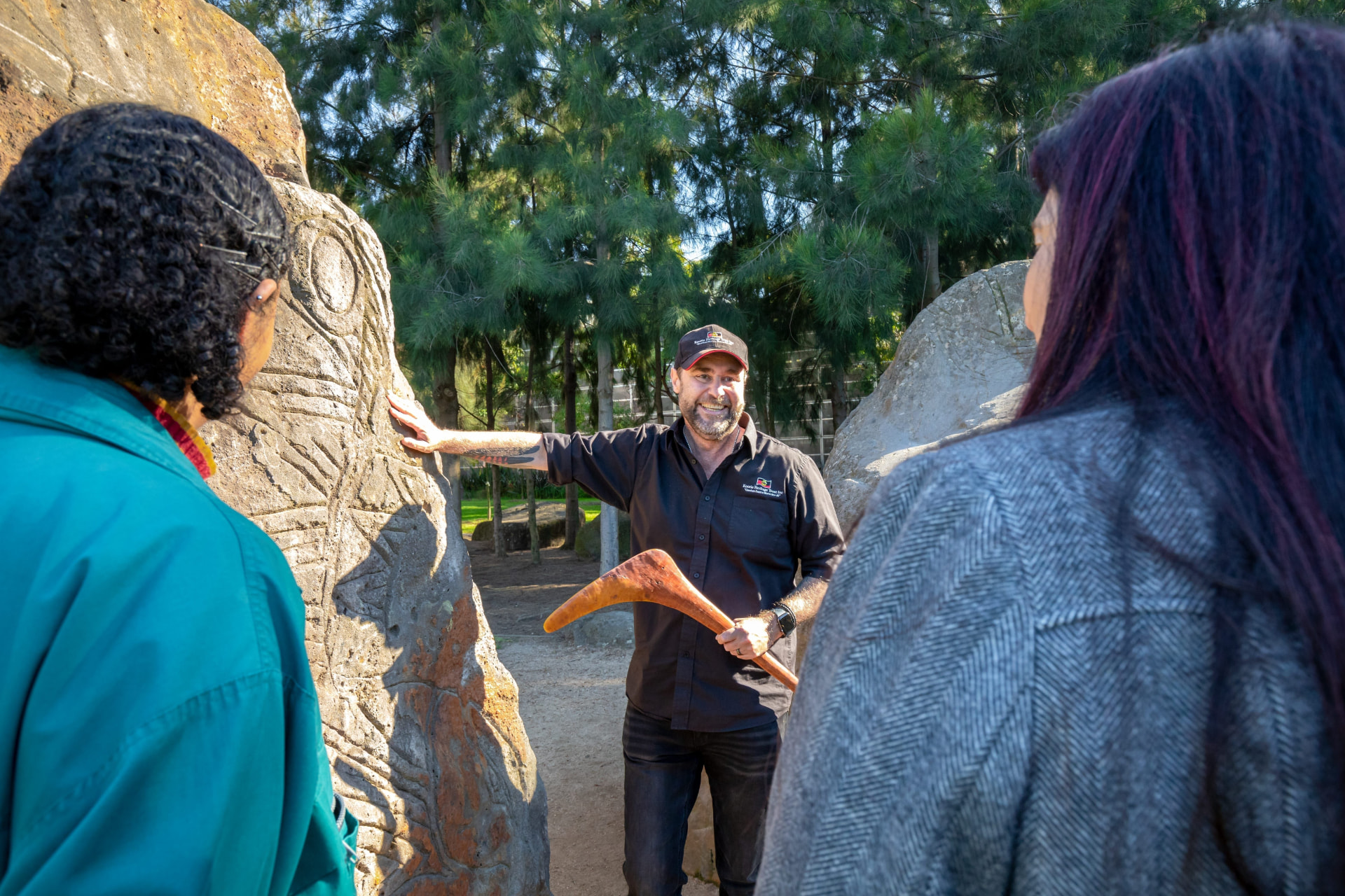 A First Nations guide with visitors beside a carved tree at Koorie Heritage Trust.