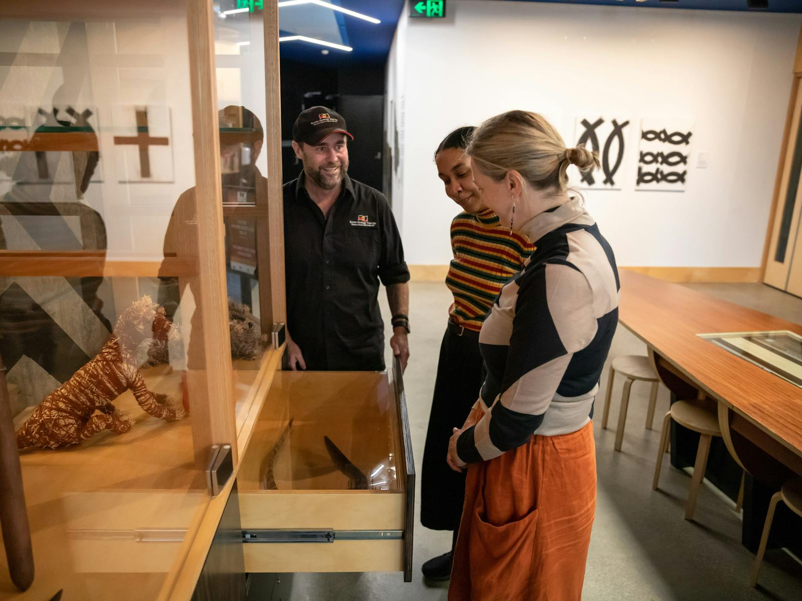A guide showing visitors First Nations objects and artefacts in display cabinets at Koorie Heritage Trust.