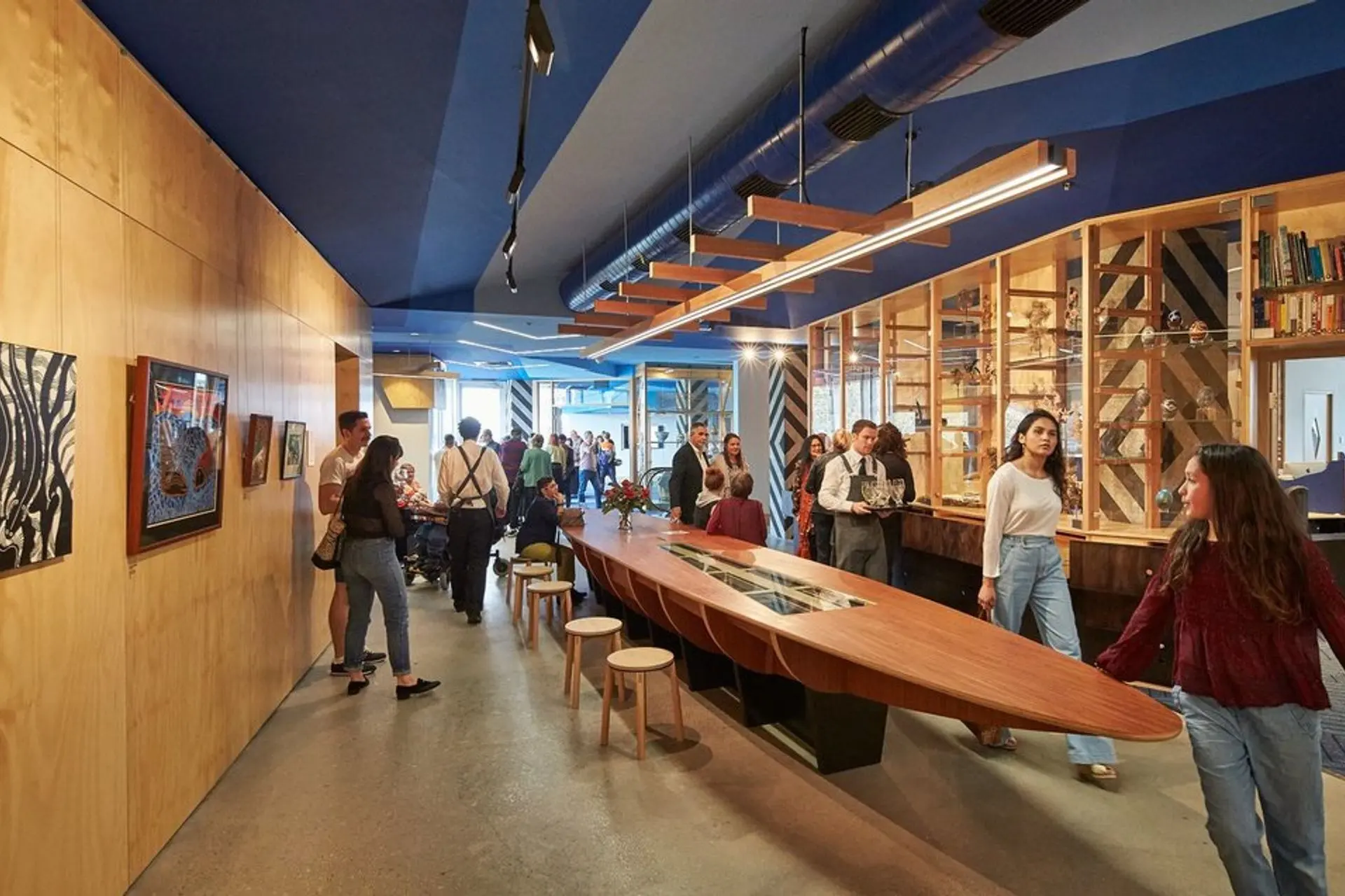 Visitors exploring the Koorie Heritage Trust gallery, with artworks and display cases along a timber wall.